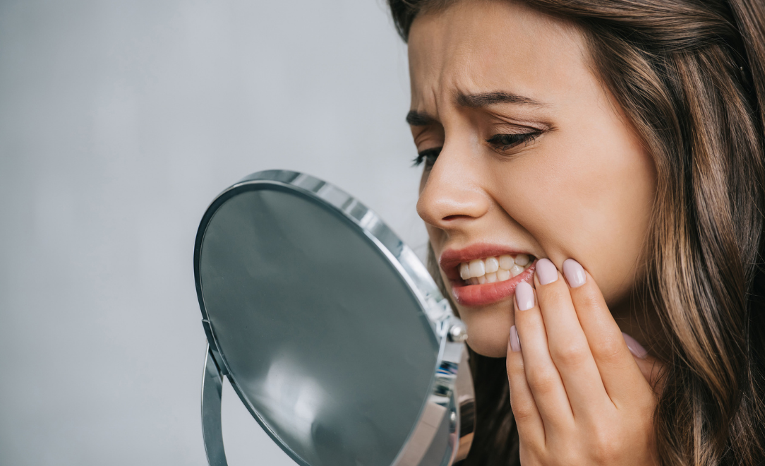 Woman looking in mirror with aching dental implant
